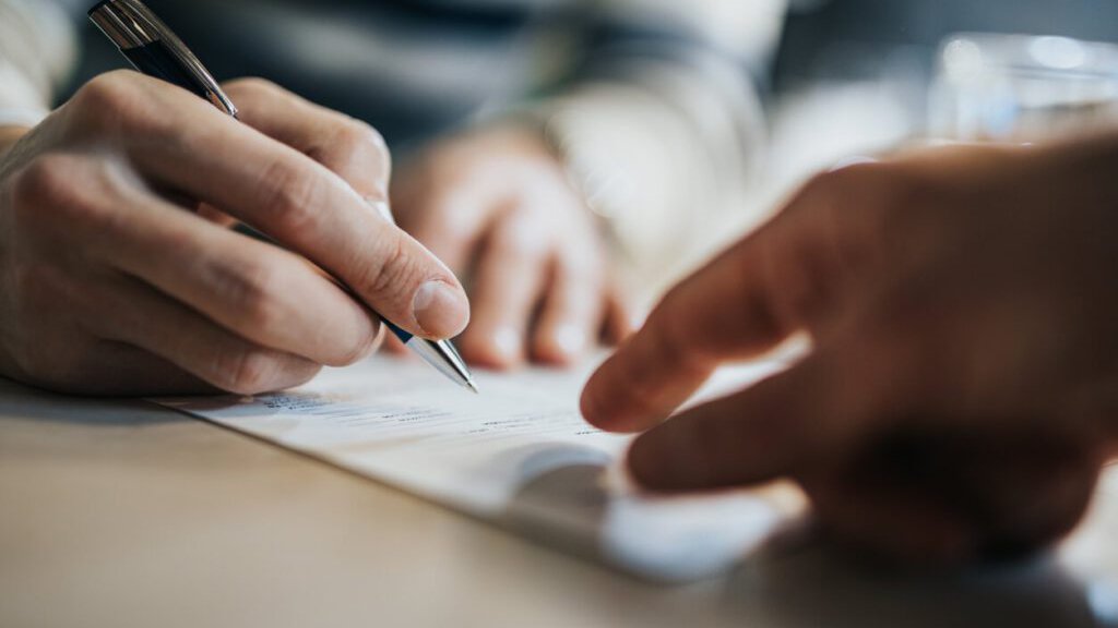 Person signing business contract document with pen during agreement or financial transaction