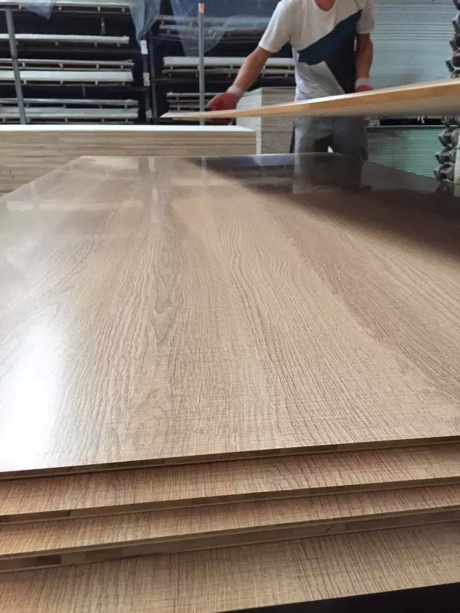 Worker handling laminated plywood boards in factory production line with wood grain surface